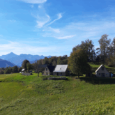 Paysage de montagne avec des petites maisons en fond, avec à l'arrière-plan des montagnes
