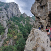 groupe de randonneurs sur un sentier perché en montagne avec un paysage montagnard entre roche et arbres