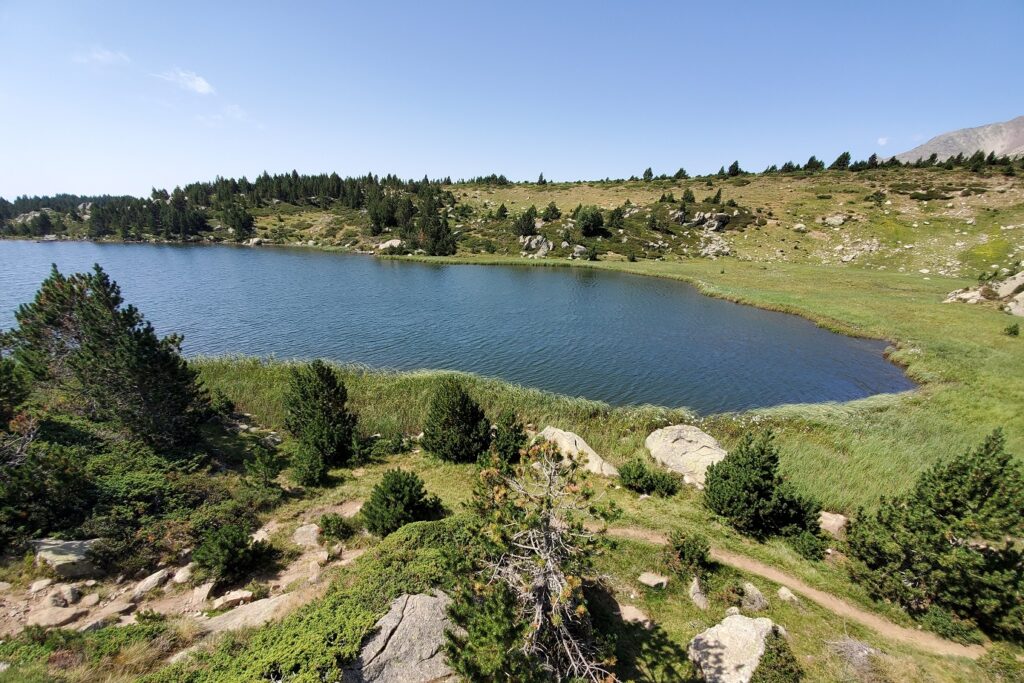Lac de montagne en contrebas de la prise de vue, avec un sentier passant devant une roche