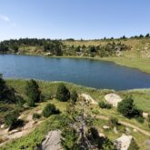 Lac de montagne en contrebas de la prise de vue, avec un sentier passant devant une roche
