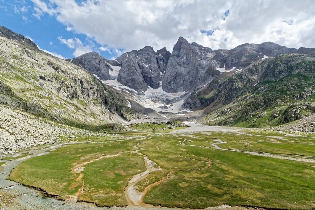 Paysage de montagne avec le Vignemale en fond, une grande plaine sur le devant marquée de sentiers.