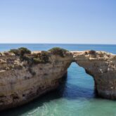 Paysage littoral avec de l'eau aux couleurs turquoises et un pont naturel en pierre passant au-dessus