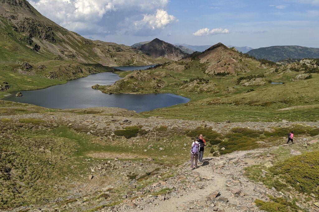 Groupe de randonneurs sur un sentier en direction d'un lac de montagne entouré de montagnes