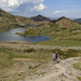 Groupe de randonneurs sur un sentier en direction d'un lac de montagne entouré de montagnes