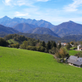 Paysage estival de montagne avec en fond des sommets et des reliefs montagneux, et au premier plan une plaine en herbe
