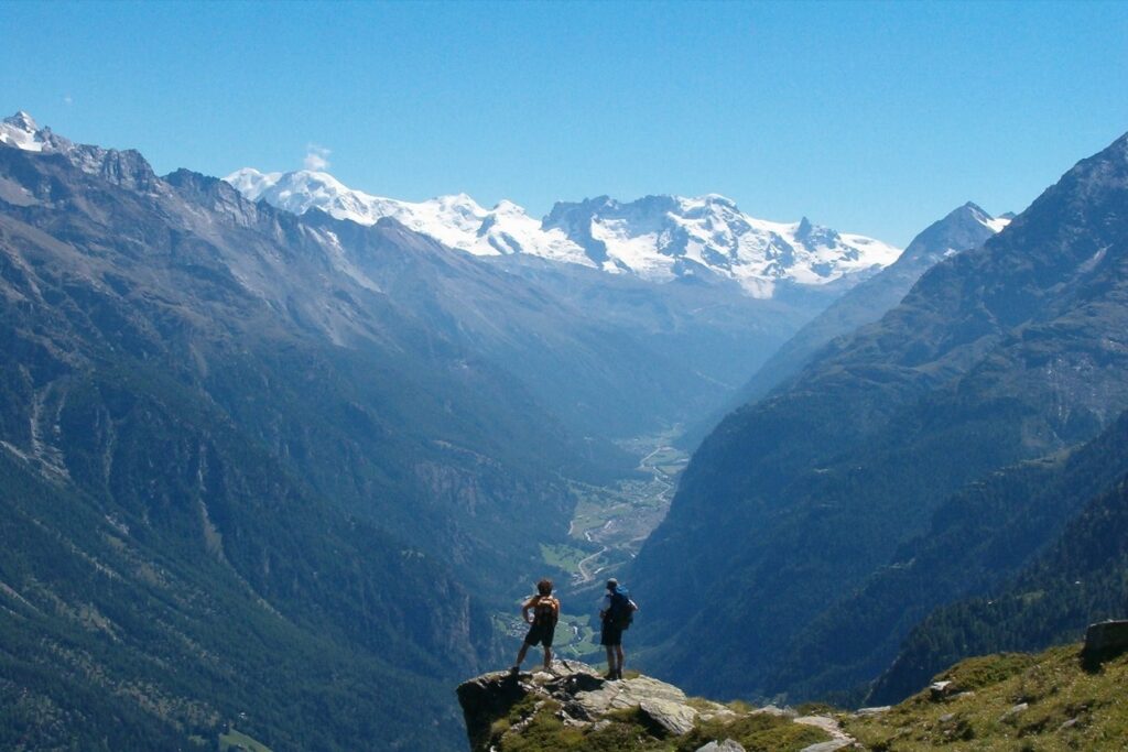 Deux randonneurs sur un rocher face aux différents sommets, face à eux, sur la haute route de Chamonix-Zermatt