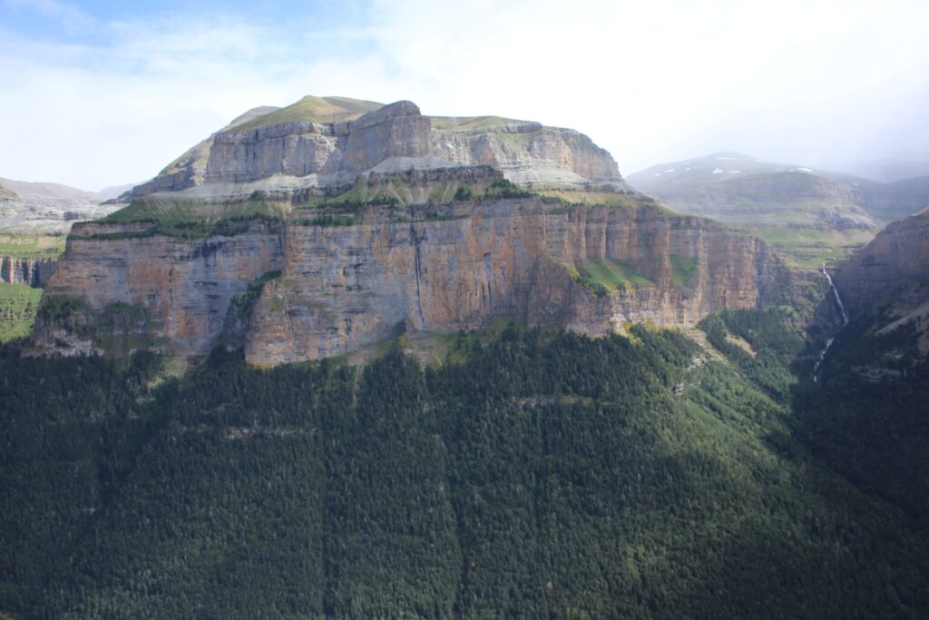 prise de vue d'une montagne avec une cascade sur la droite et le pied de la montagne est recouvert de forêt
