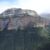 prise de vue d'une montagne avec une cascade sur la droite et le pied de la montagne est recouvert de forêt