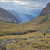 Groupe de randonneurs sur un sentier en train de monter avec derrière eux de nombreux sommets et des rayons de soleil qui passent à travers les nuages