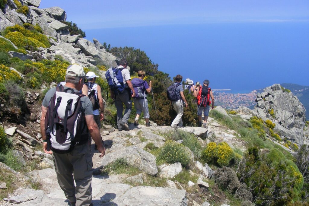 Groupe de randonneurs sur un sentier de pierre qui descend vers des petits villages ainsi que la mer