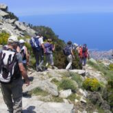 Groupe de randonneurs sur un sentier de pierre qui descend vers des petits villages ainsi que la mer