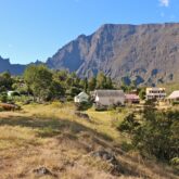 Paysage montagnard sur l'île de la Réunion avec au premier plan des champs et des maisons et à l'arrière-plan un sommet