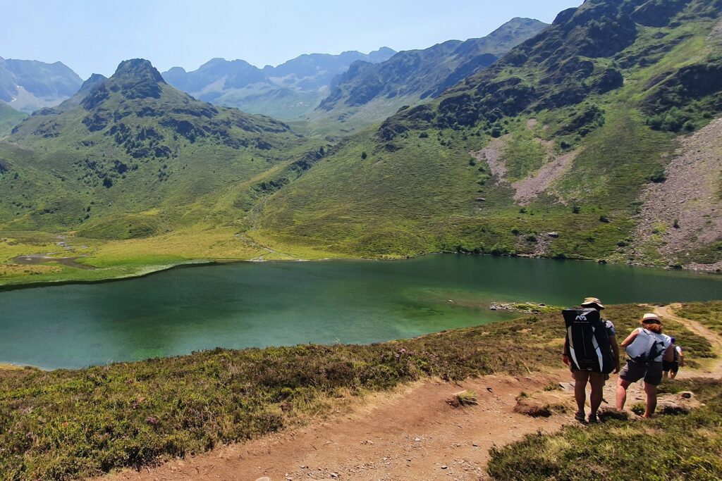 Paysage de montagne avec un sentier sur lequel un groupe de marcheurs avance et un lac sur la gauche