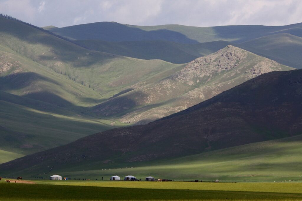 Paysage de montagne avec une plaine en bas, avec des yourtes et des chevaux