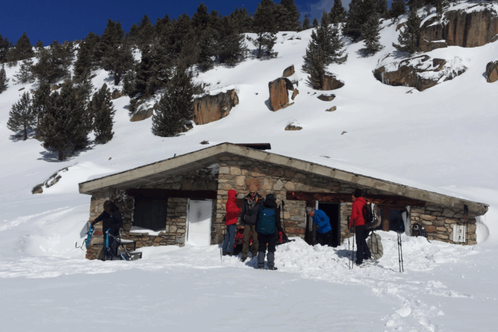 Groupe de randonneurs en raquettes dans un paysage enneigé devant une maison en pierre.