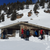 Groupe de randonneurs en raquettes dans un paysage enneigé devant une maison en pierre.