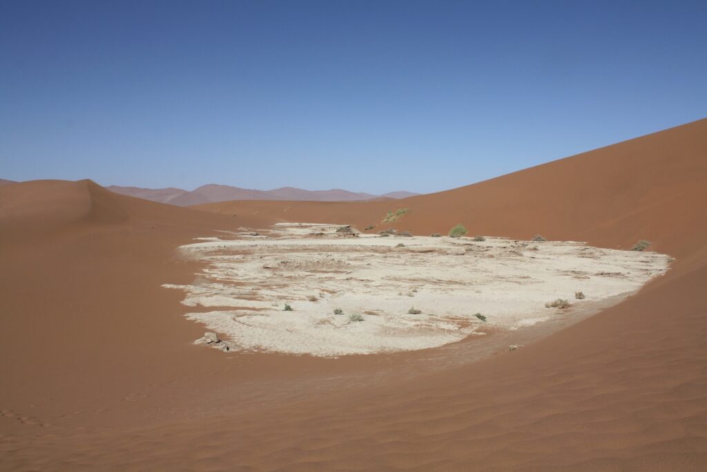 Paysage désertique avec du sable de couleur marron ainsi qu'une zone de sable blanc, sous le ciel bleu de Namibie.