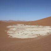 Paysage désertique avec du sable de couleur marron ainsi qu'une zone de sable blanc, sous le ciel bleu de Namibie.