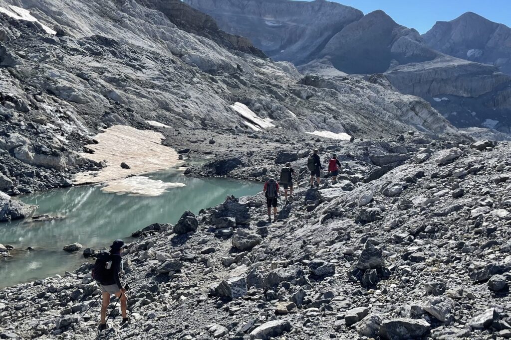 Groupe de randonneurs entre les posets et l'Aneto face à un lac de montagne dans un espace très rocailleux