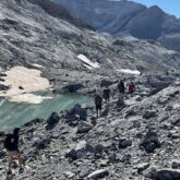 Groupe de randonneurs entre les posets et l'Aneto face à un lac de montagne dans un espace très rocailleux