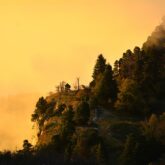Paysage montagnard avec un ciel aux couleurs jaunes dues au soleil et des arbres placés de part et d'autre.