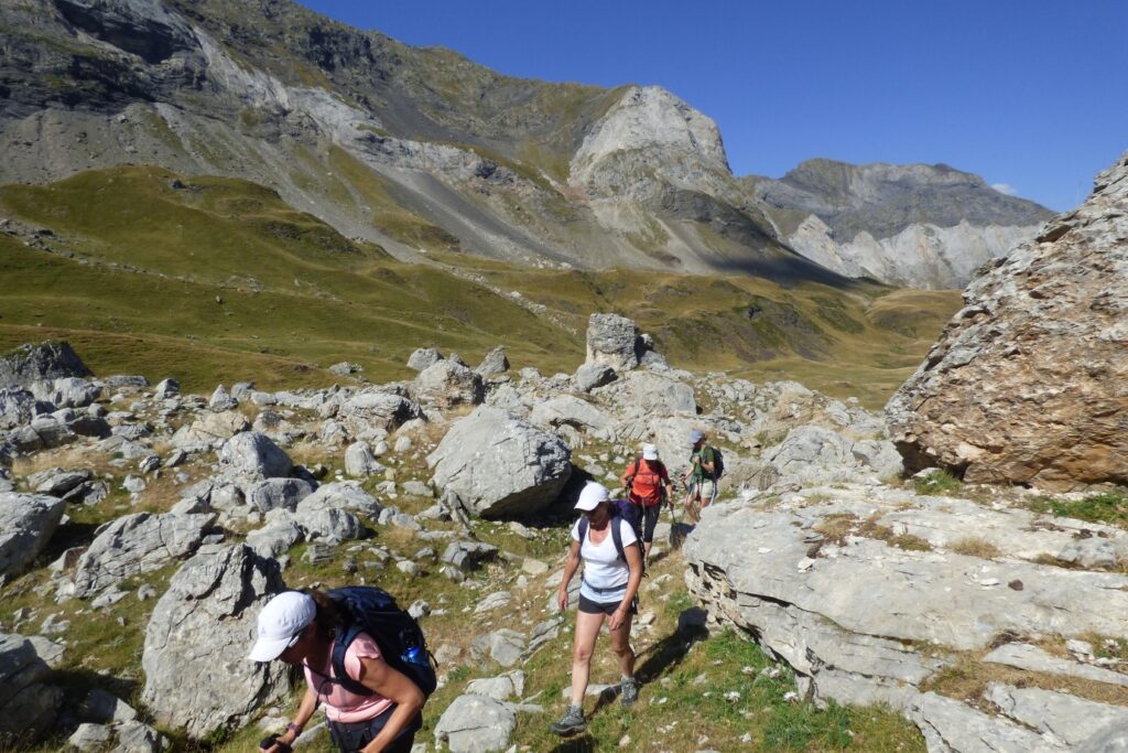 Groupe de randonneurs montant à flanc d'une montagne entre les roches avec différents sommets derrière