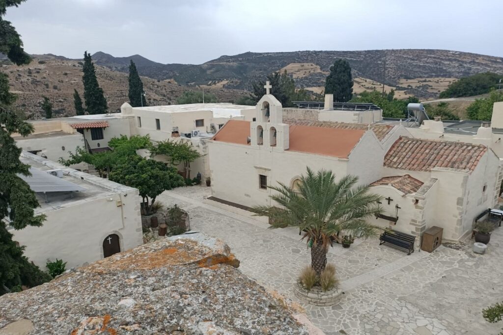 Photo d'un lieu d'habitation en Crète avec des bâtiments aux couleurs blanches ainsi que des palmiers dans la cour intérieure