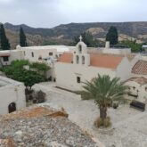 Photo d'un lieu d'habitation en Crète avec des bâtiments aux couleurs blanches ainsi que des palmiers dans la cour intérieure