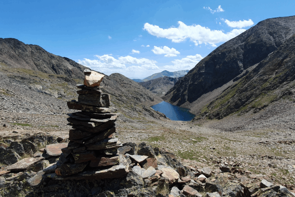 Paysage de montagne avec un cairn en premier plan et, au second plan, en contrebas, un lac bleu.