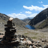 Paysage de montagne avec un cairn en premier plan et, au second plan, en contrebas, un lac bleu.