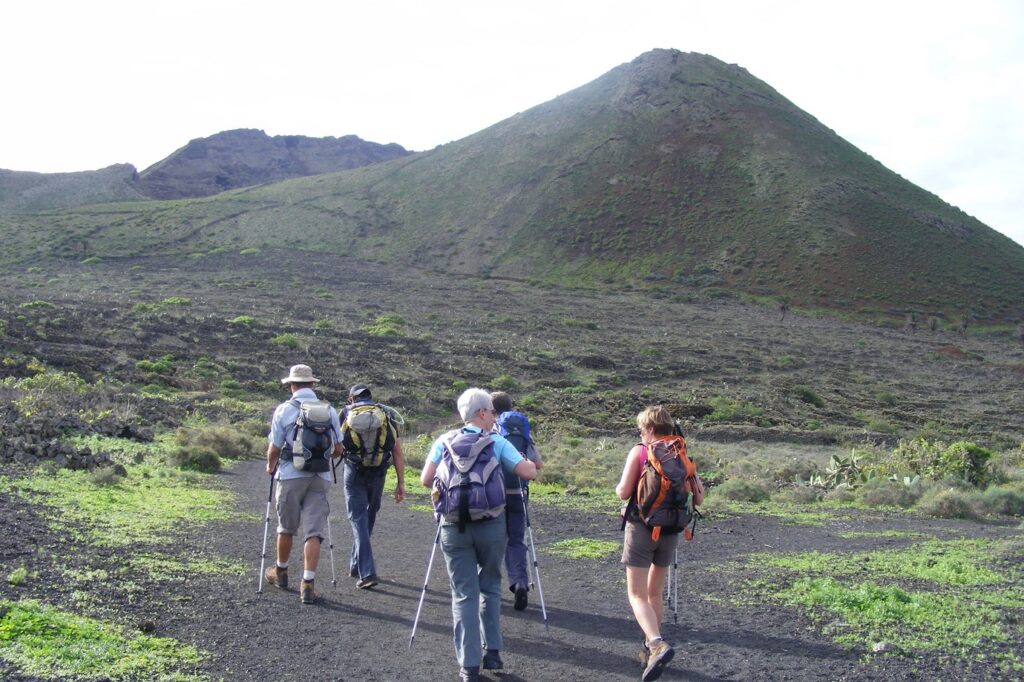 groupe de randonneurs sur un chemin de terre noire dû à la présence de volcans lors d'une randonnée vers le mont Corona dans les canaries