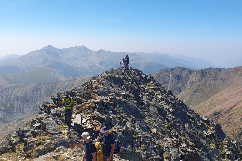 Groupe de randonneurs au sommet d'une montagne, face à un paysage montagnard où l'on voit des sommets à l'horizon.