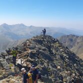 Groupe de randonneurs au sommet d'une montagne, face à un paysage montagnard où l'on voit des sommets à l'horizon.