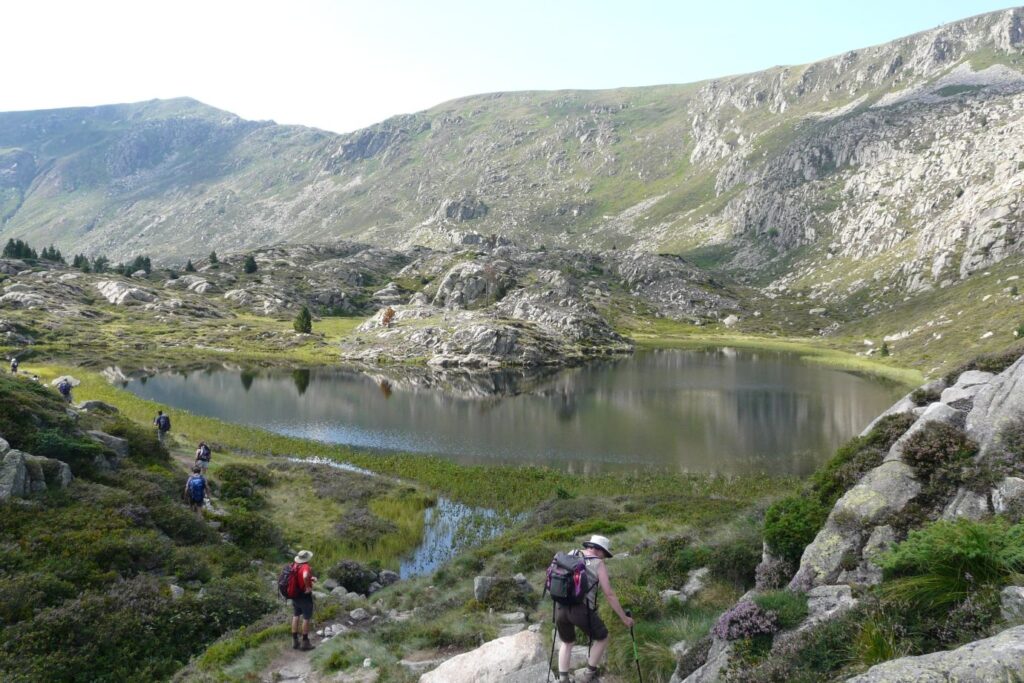 groupe de randonneurs accédant à un lac de montagne, sur un sentier avec en fond des sommets montagneux