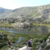 groupe de randonneurs accédant à un lac de montagne, sur un sentier avec en fond des sommets montagneux