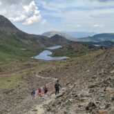 Groupe de randonneurs sur un sentier se dirigeant vers une étendue d'eau à travers les montagnes lors de l'étape 8 de la HRP