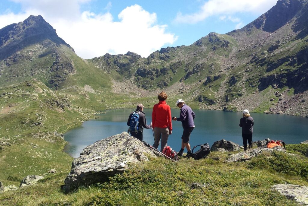 Groupe de randonneurs face à un lac de montagne et des sommets en face.