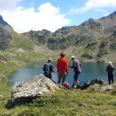 Groupe de randonneurs face à un lac de montagne et des sommets en face.