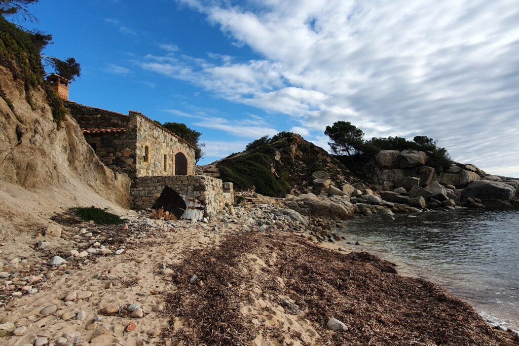 Paysage de bord de mer avec une plage de cailloux ainsi qu'une maison en pierre