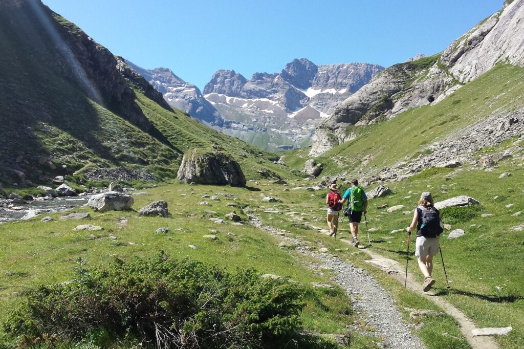 Groupe de randonneurs sur un sentier entre Gavarne et Cauterets encadré par des sommets, un temps estival ainsi que de la végétation variée