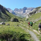 Groupe de randonneurs sur un sentier entre Gavarne et Cauterets encadré par des sommets, un temps estival ainsi que de la végétation variée