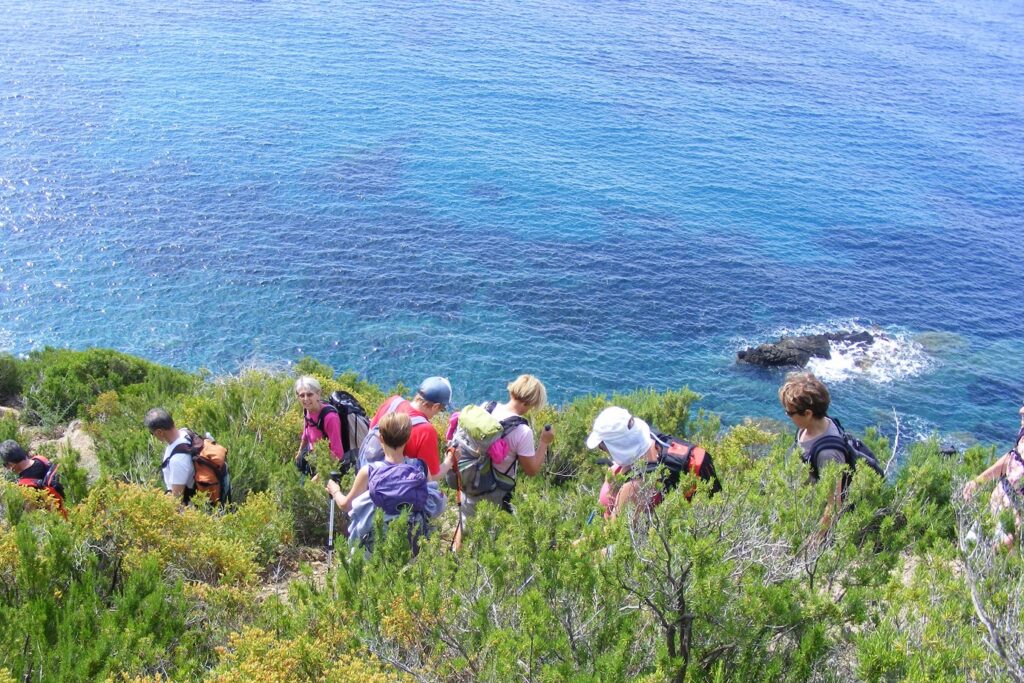 Groupe de randonneurs sur un sentier à flanc de montagne en train de descendre un sentier avec la mer en contrebas sur l'île d'Elbe