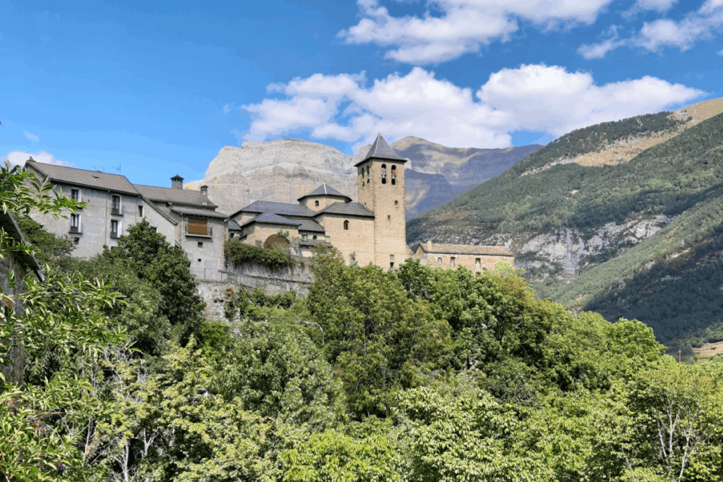 Village perché sur les hauteurs, entouré de végétation et d'arbres, avec des sommets derrière.
