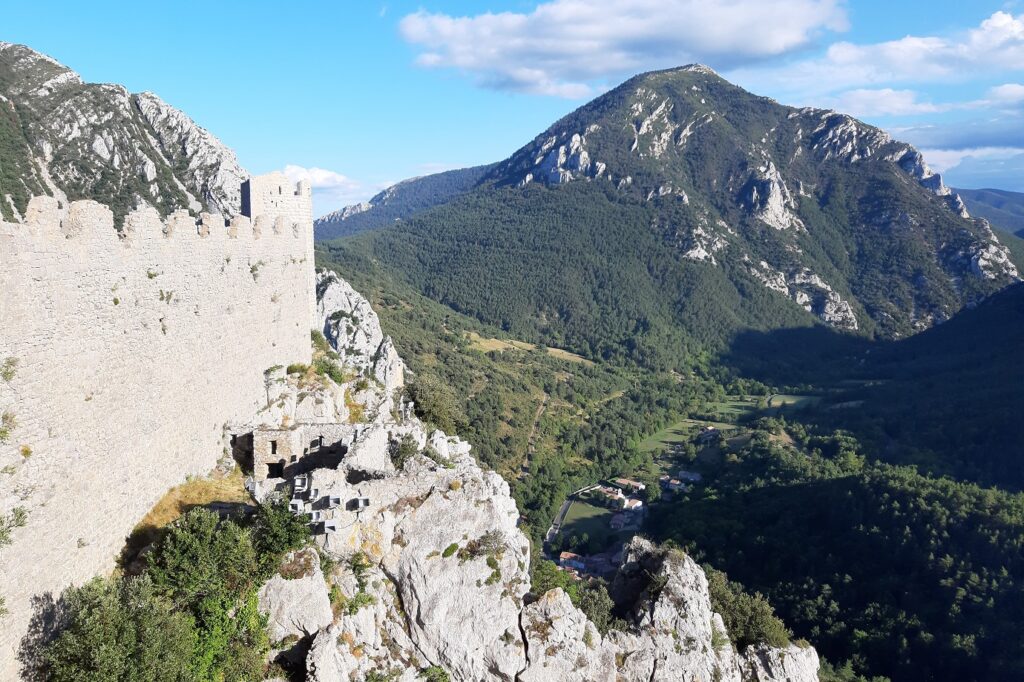 Paysage Cathare avec un château et en contrebas une vallée, en arrière-plan un sommet recouvert d'arbres