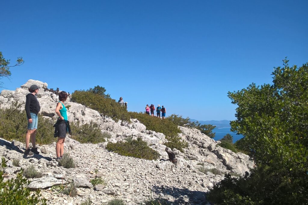 Groupe de randonneurs sur des sentiers en montagne à travers les cailloux, avec en contrebas la mer