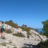 Groupe de randonneurs sur des sentiers en montagne à travers les cailloux, avec en contrebas la mer