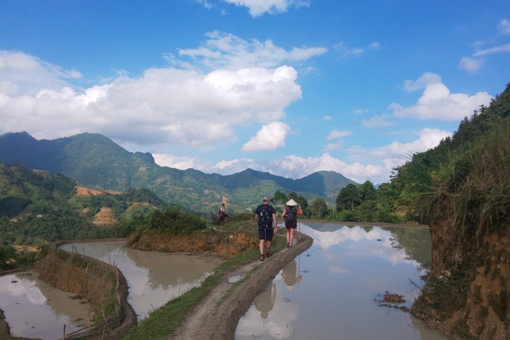 Groupe de personnes qui marchent vers les montagnes sur un sentier de terre battue encadré par des rizières.