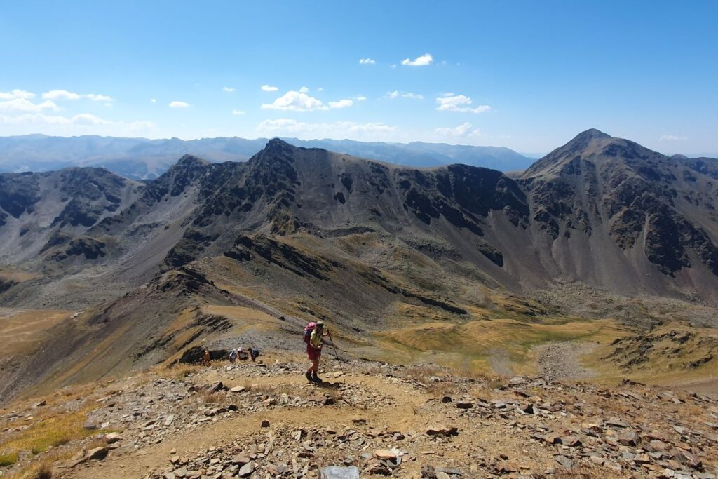 Montagnard qui monte un sommet d'Andorre avec derrière lui une rangée de sommets.