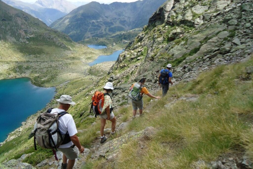 Groupe de randonneurs à flanc de la montagne, il y a une série de lacs en contrebas. Ils font une randonnée en Andorre.