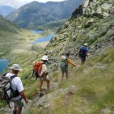 Groupe de randonneurs à flanc de la montagne, il y a une série de lacs en contrebas. Ils font une randonnée en Andorre.